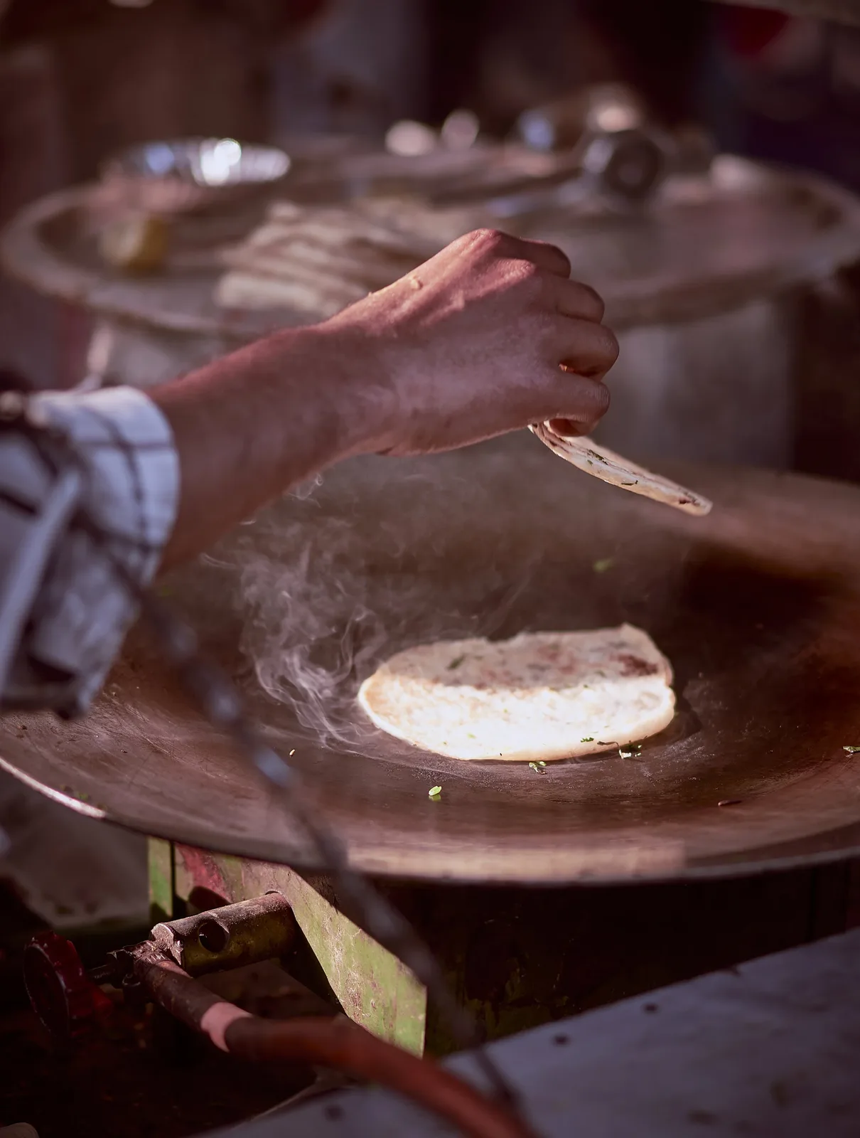 Chef hand-pressing naan on a hot griddle
